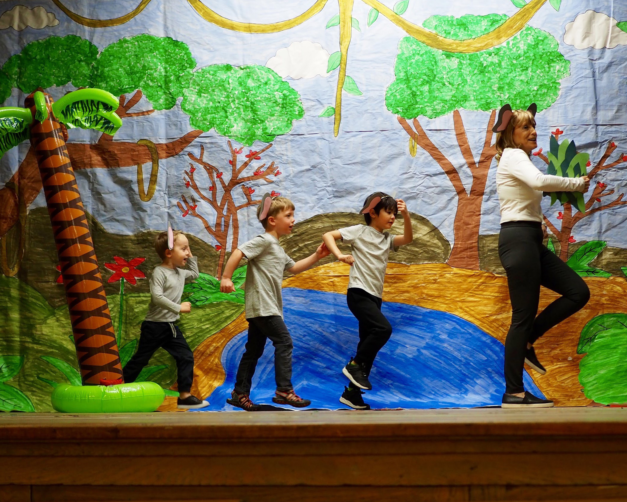 teacher on stage with 3 children marching. All wearing elephant ears.